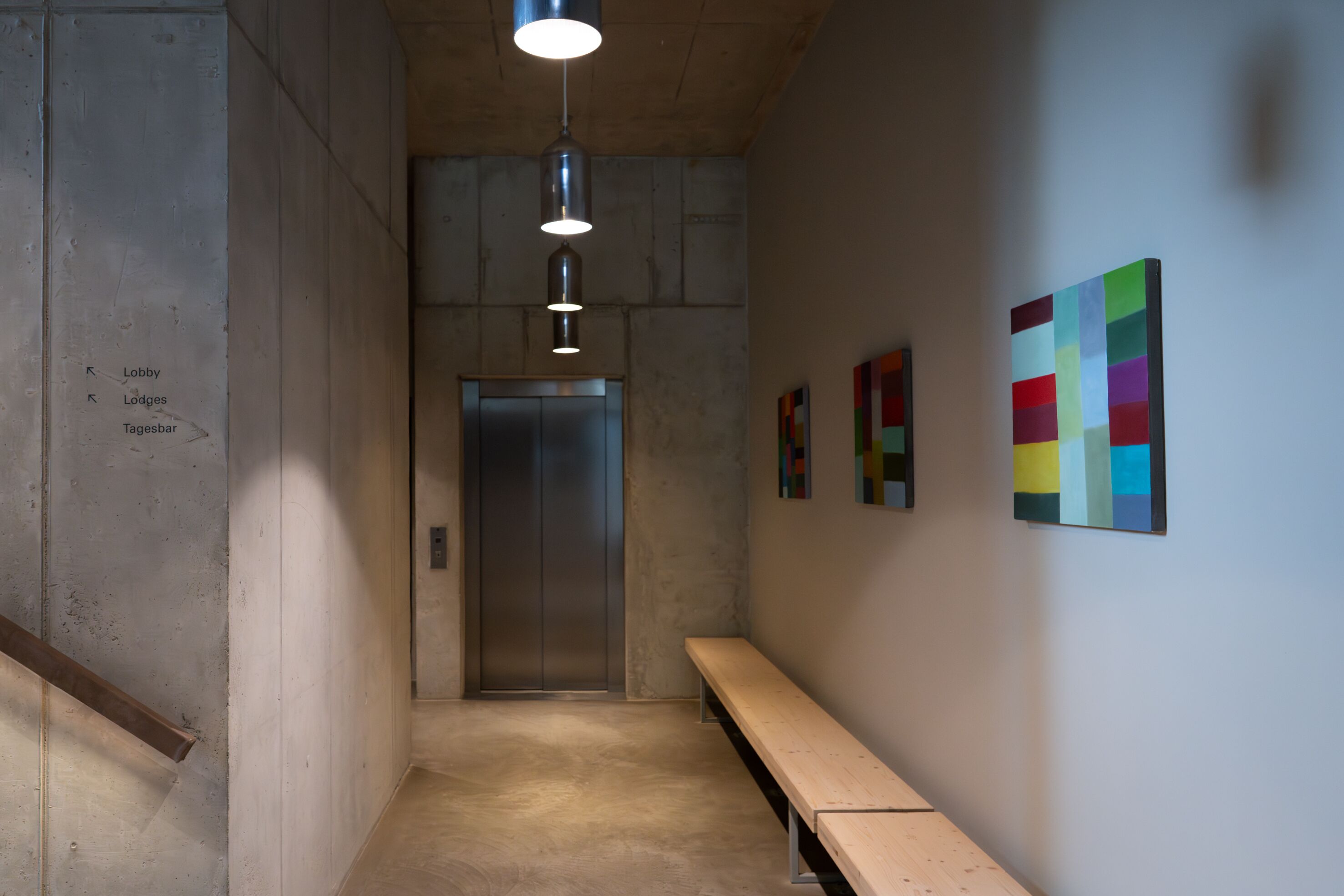 A hallway with a bench, an elevator, and colorful artwork on the wall.