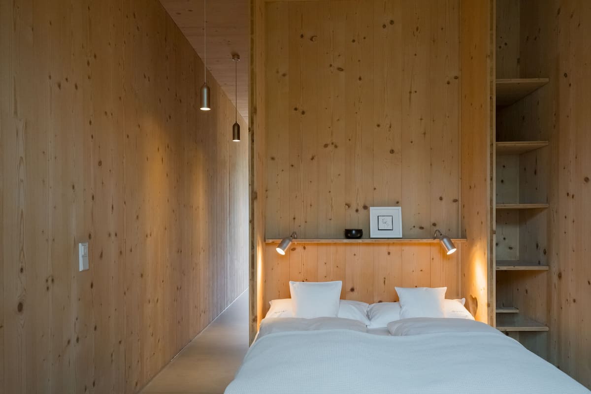 Ein Schlafzimmer mit Holzwand, einem Bett mit weißer Bettwäsche, einem Regal mit Bilderrahmen und einem kleinen Tisch mit einer Schale.
