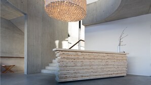 A modern interior with a large wooden reception desk, a unique textured hanging light fixture, and a minimalist staircase.