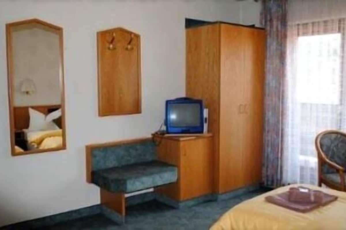 A hotel room with a bed, a small desk with a television, a wardrobe, and a mirror.