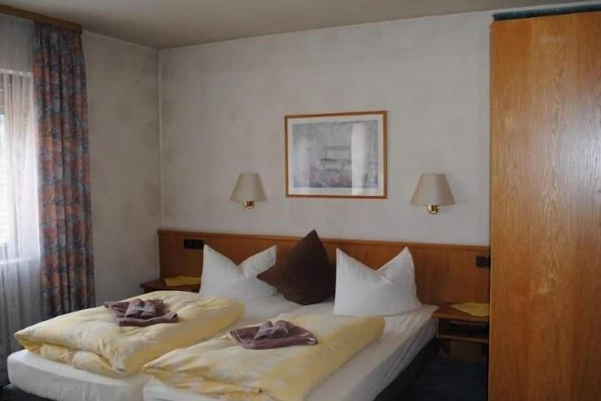 A hotel room with a bed, two bedside lamps, a framed picture on the wall, and a wooden wardrobe.