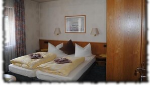 A hotel room with a double bed, two bedside tables, a wooden headboard, a framed picture on the wall, and a door. - Gasthof Stern (Burgsinn)