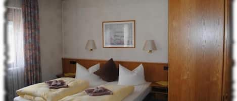 A hotel room with a double bed, two bedside tables, a wooden headboard, a framed picture on the wall, and a door.