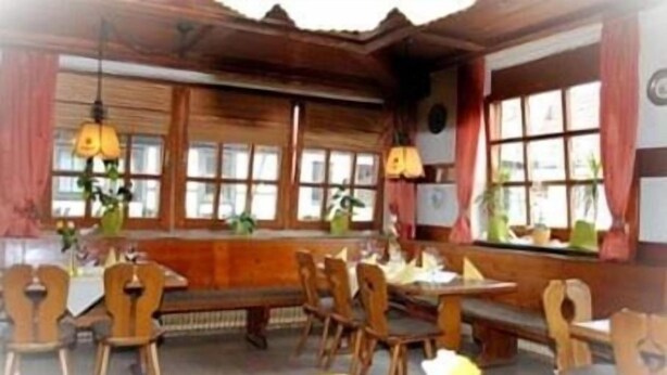 A traditional wooden interior with a long bench and multiple chairs, large windows, and hanging lamps. - Gasthof Stern (Burgsinn)