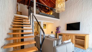 Una escalera con peldaños de madera y barandilla de metal, un sofá gris, un armario de madera y un televisor de pantalla plana en la pared.
