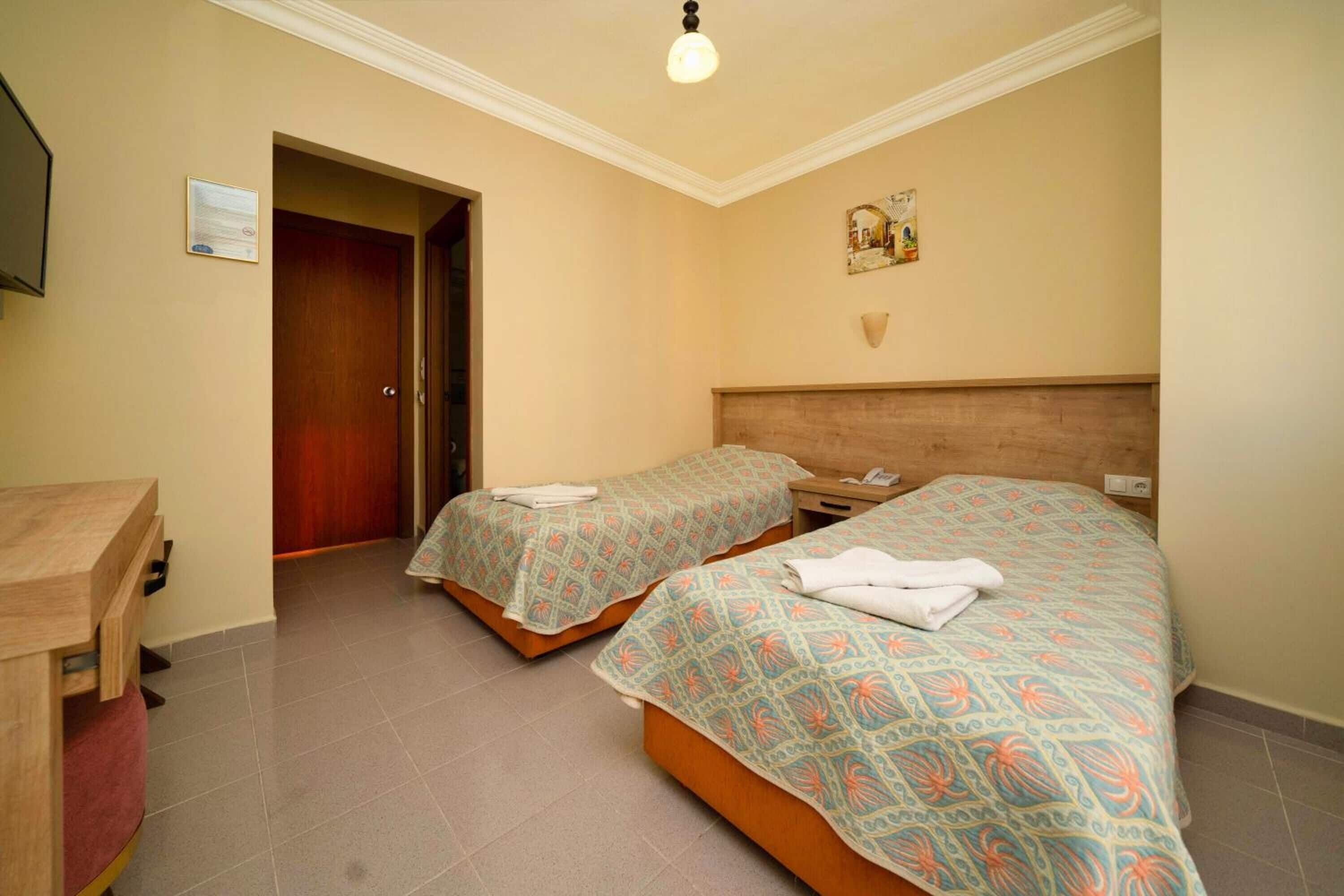 Ein Hotelzimmer mit zwei Betten, einem Schreibtisch und einer Tür zu einem weiteren Raum.