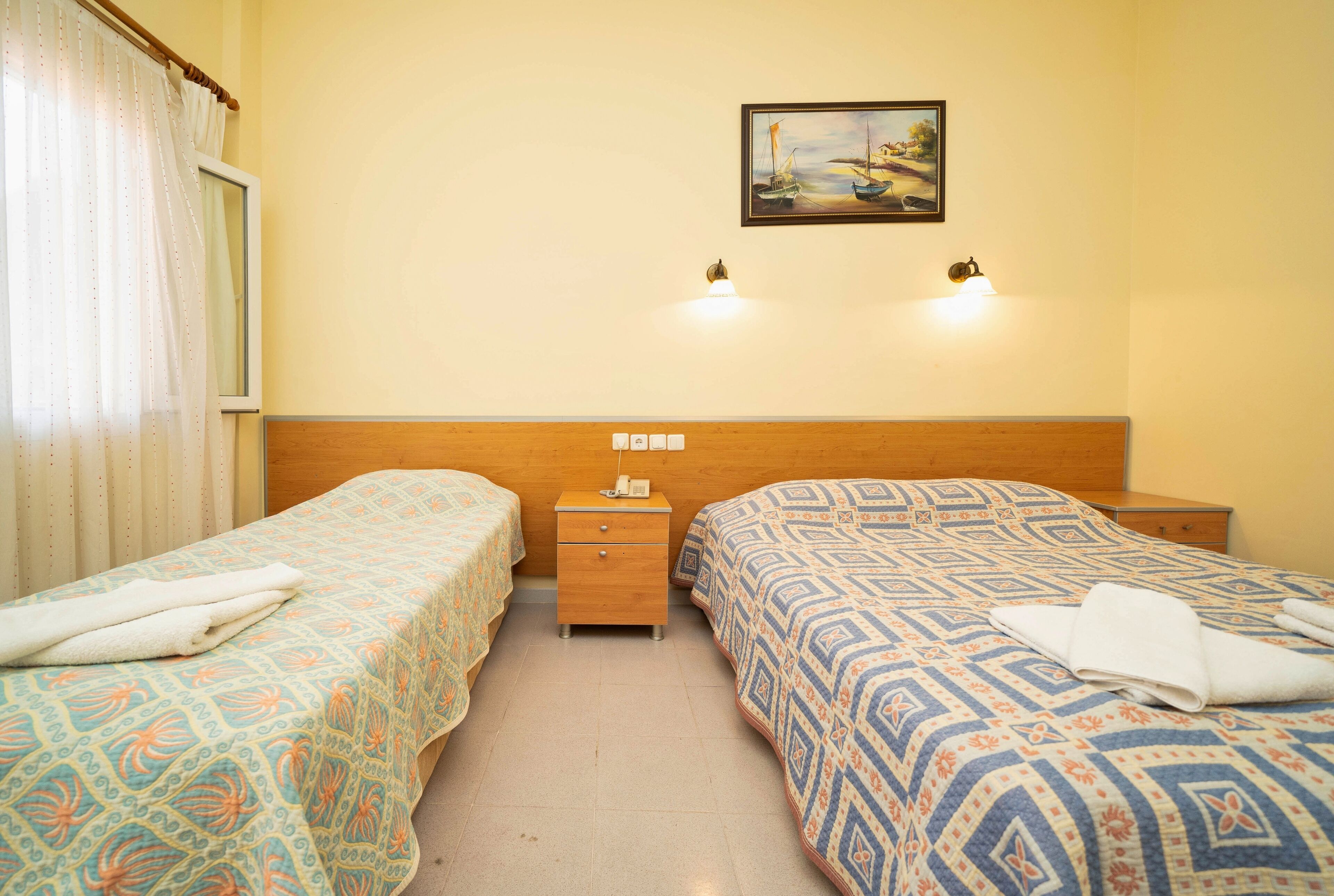 Een hotelkamer met twee enkele bedden, een houten hoofdbord, een nachtkastje met een telefoon en een schilderij aan de muur.