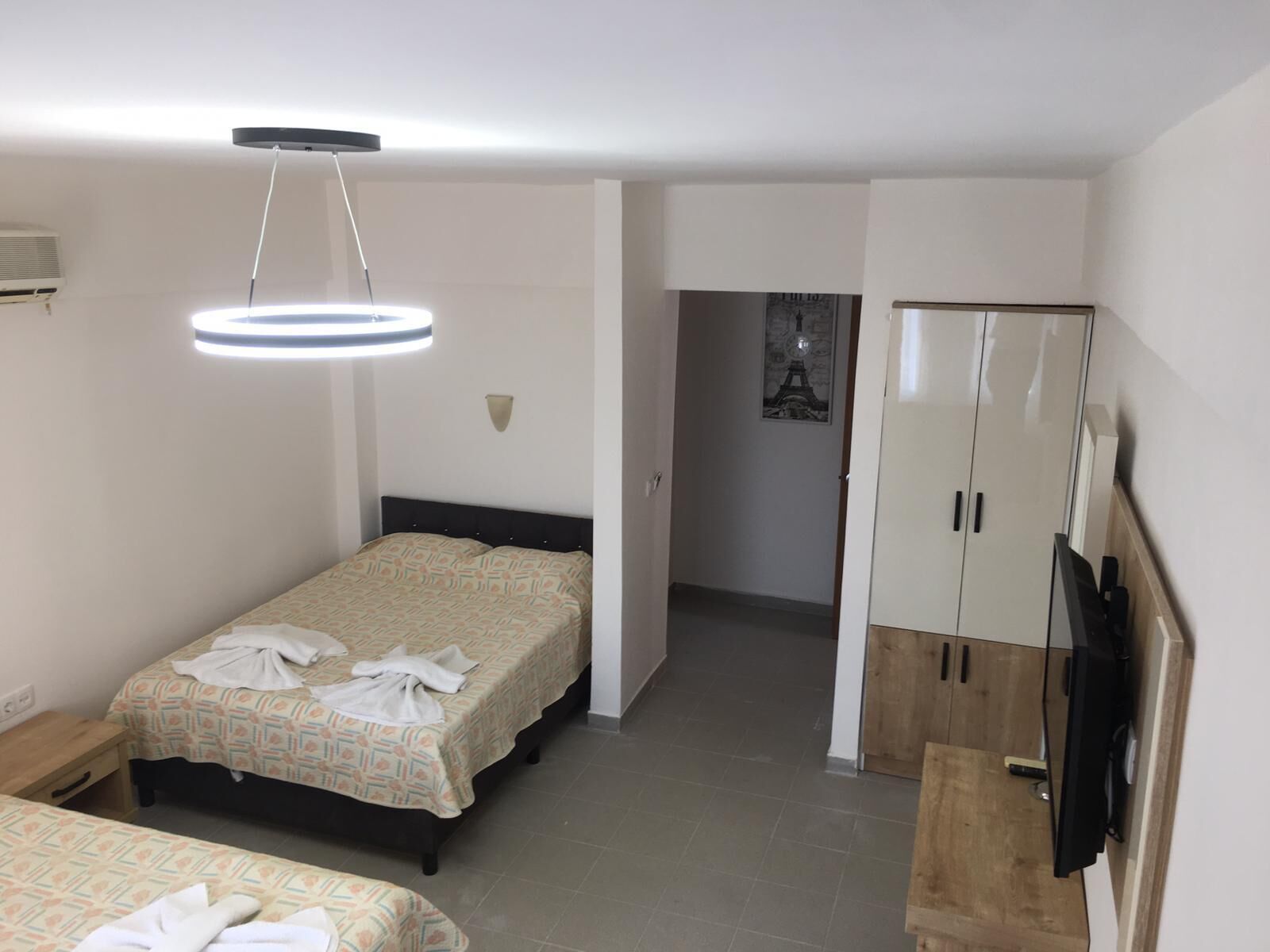 A hotel room with two beds, a wardrobe, a television, and a ceiling light fixture.