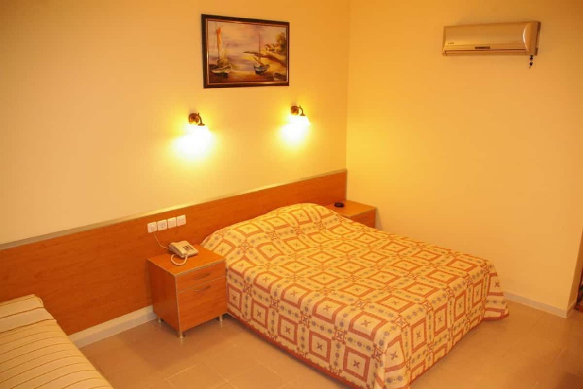 A hotel room with a wooden headboard, a patterned bedspread, a bedside table with a phone, and a wall-mounted air conditioner.