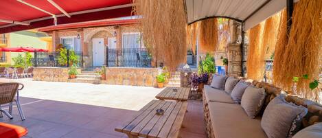 Un patio al aire libre con mesas de madera, un sofá, paredes de piedra y plantas en macetas.