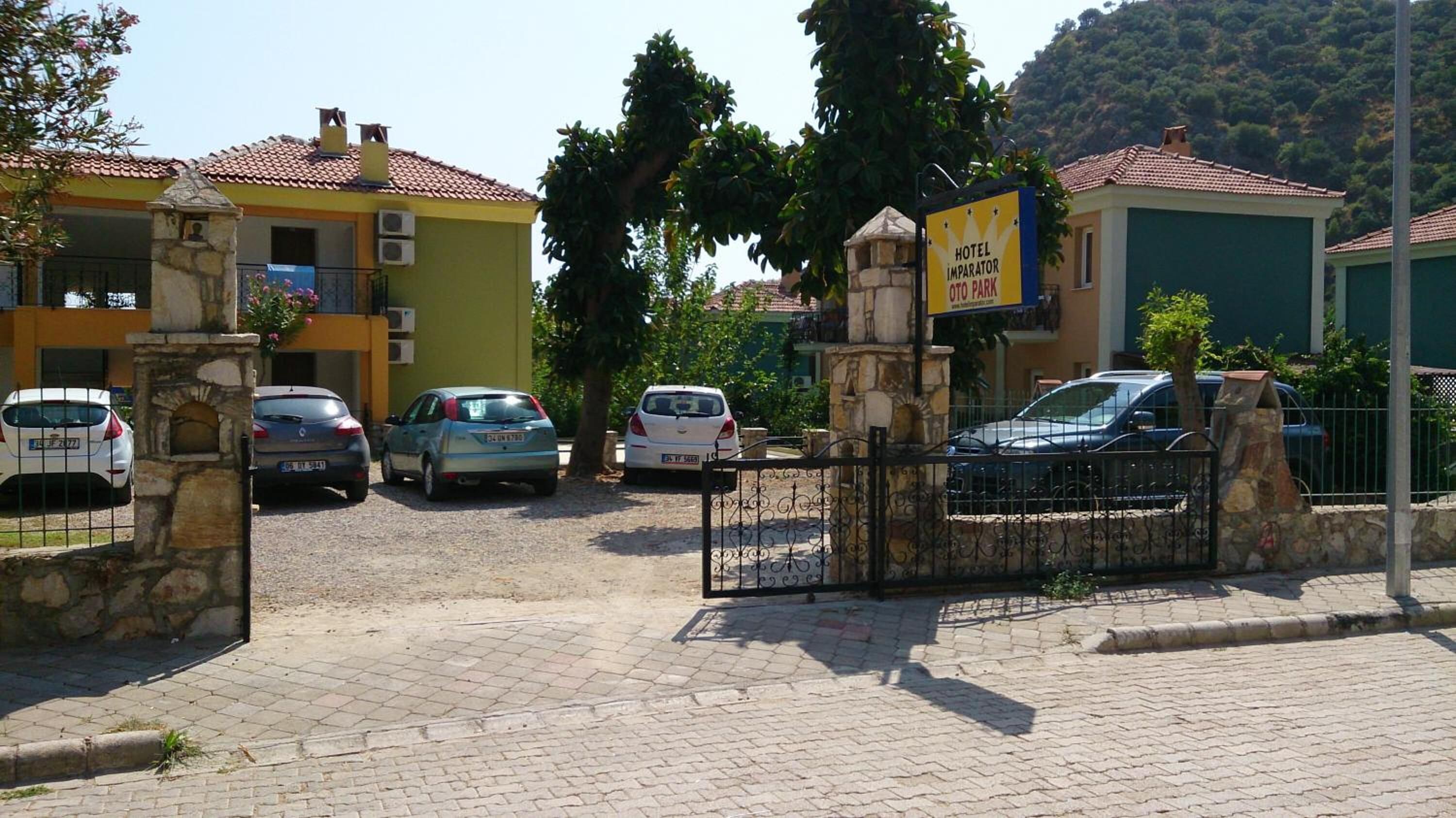 A hotel entrance with a stone gate, parked cars, and a sign indicating a parking area.