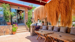 Un patio al aire libre con muros de piedra, una mesa de madera y una zona de estar con cojines.