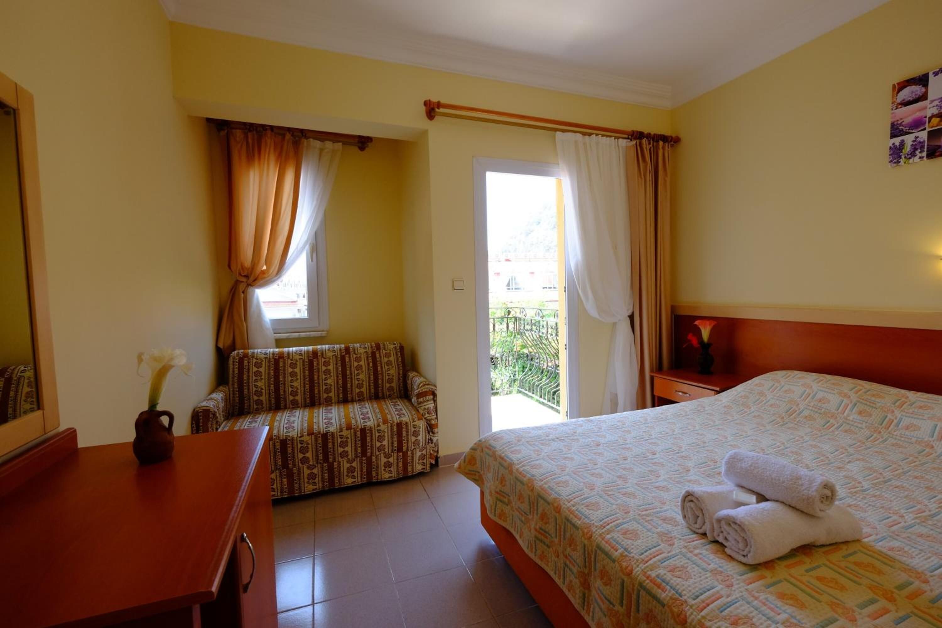 A hotel room with a bed, a sofa, a desk, and a balcony with curtains.