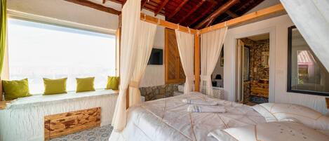 Une chambre avec un grand lit, une tête de lit en bois et une vue sur la mer.