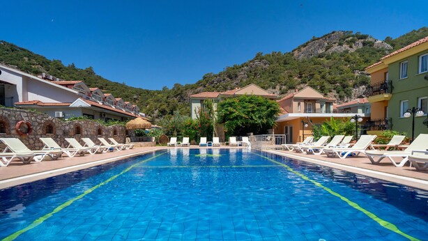 Una piscina con sillas de descanso, rodeada de edificios con balcones y un paisaje montañoso al fondo.