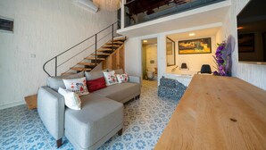 Una sala moderna con un sofá gris, una escalera de madera y una mesa grande de madera.