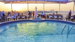 Zona de piscina con vista al atardecer y un paisaje urbano de fondo.