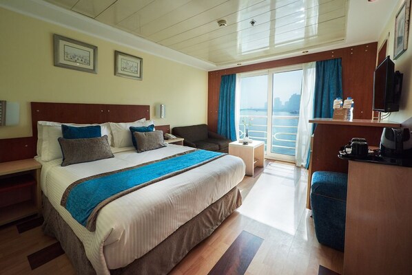 A hotel room with a large bed, a desk, a chair, a TV, and a view of the water. - Nile View Jewel Hotel (Cairo)