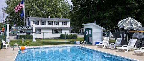 A swimming pool with lounge chairs and a small shed, surrounded by a fence and trees.