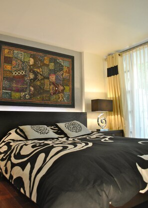 A neatly made bed with a black and white patterned bedspread, a decorative pillow, and a wall-mounted abstract painting. - Business Suites SG (Mexico City)