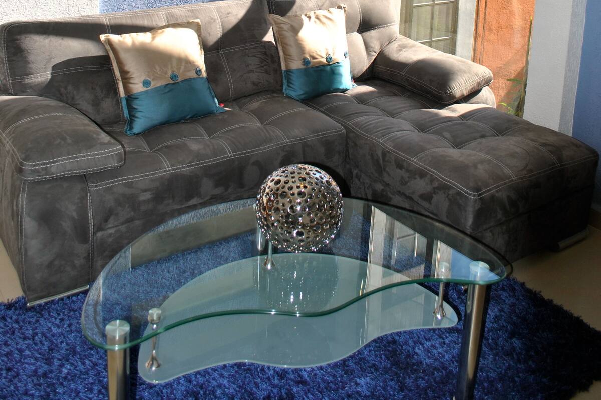 A modern living room with a grey sofa, blue cushions, a glass coffee table, and a hanging light fixture.