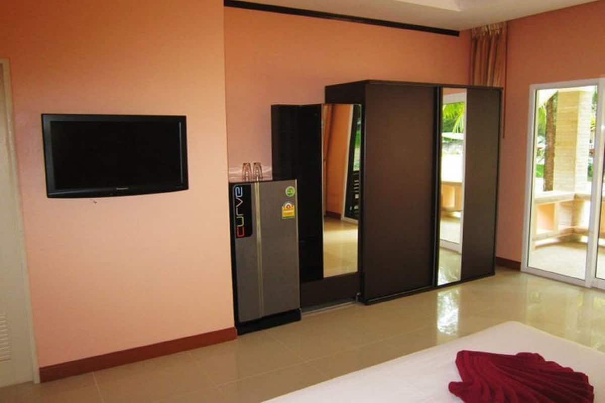 A hotel room with a flat-screen TV, minibar, sliding glass door to a balcony, and a bed with a red blanket.