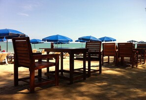 A beachside seating area with wooden chairs and tables, and blue umbrellas providing shade. - Ao Thong Beach Bungalows & Restaurant (Takua Pa)
