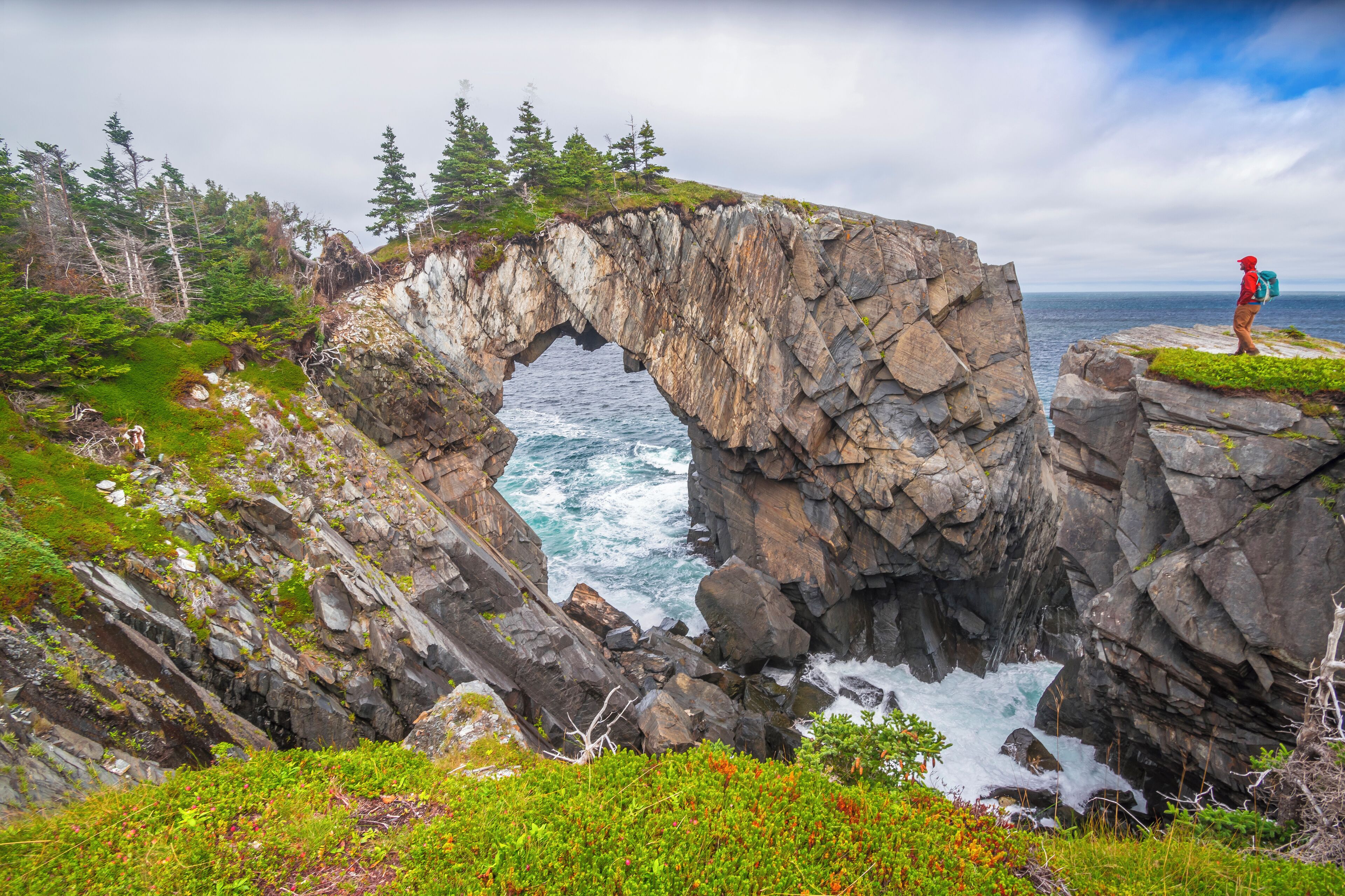 A natural rock arch formation with a person standing on a nearby cliff.