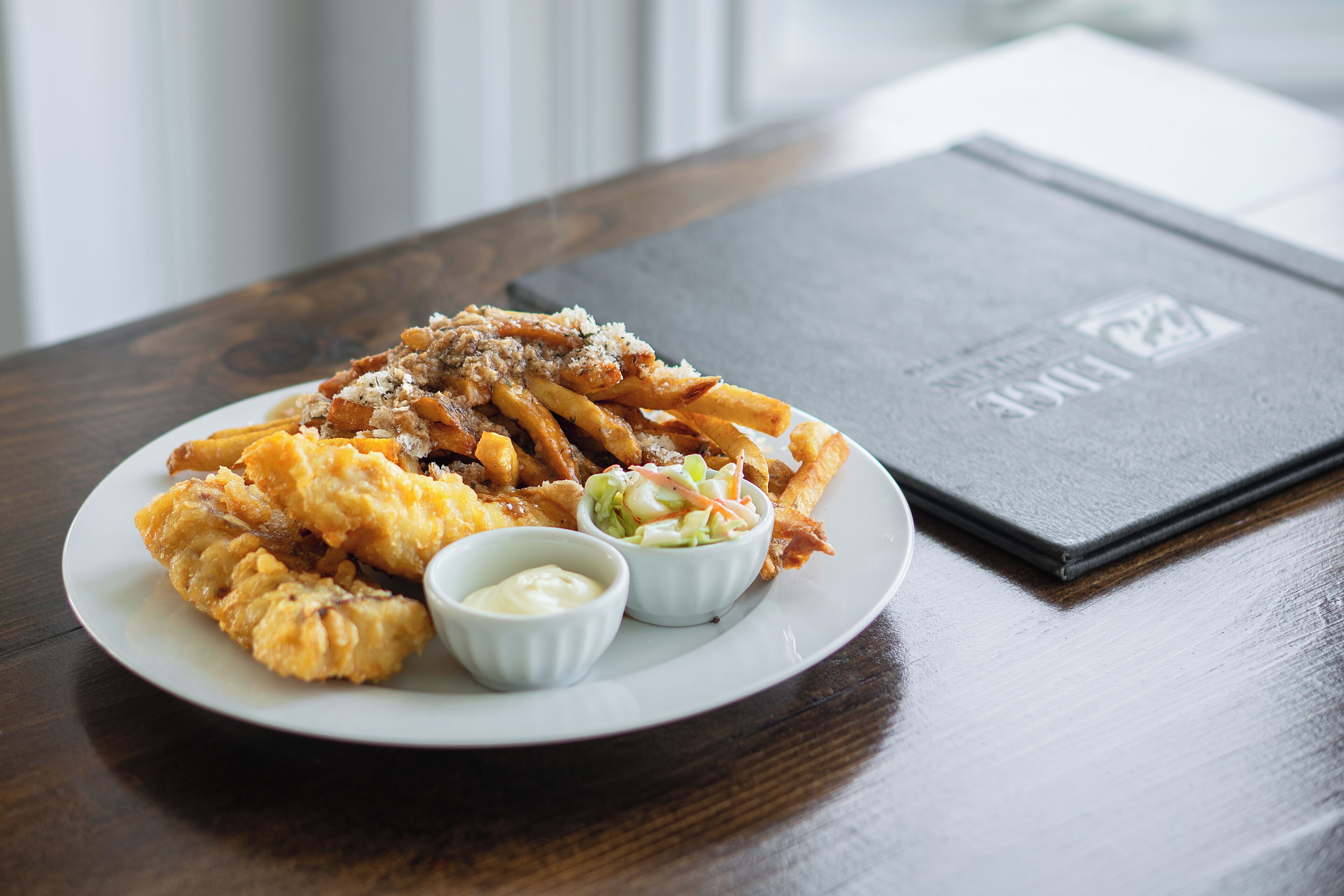 A plate of food with fries, coleslaw, and a small bowl of sauce on a wooden table.