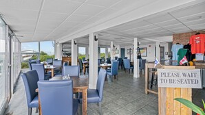 A restaurant with outdoor seating, tables, chairs, and a sign indicating wait for seating.