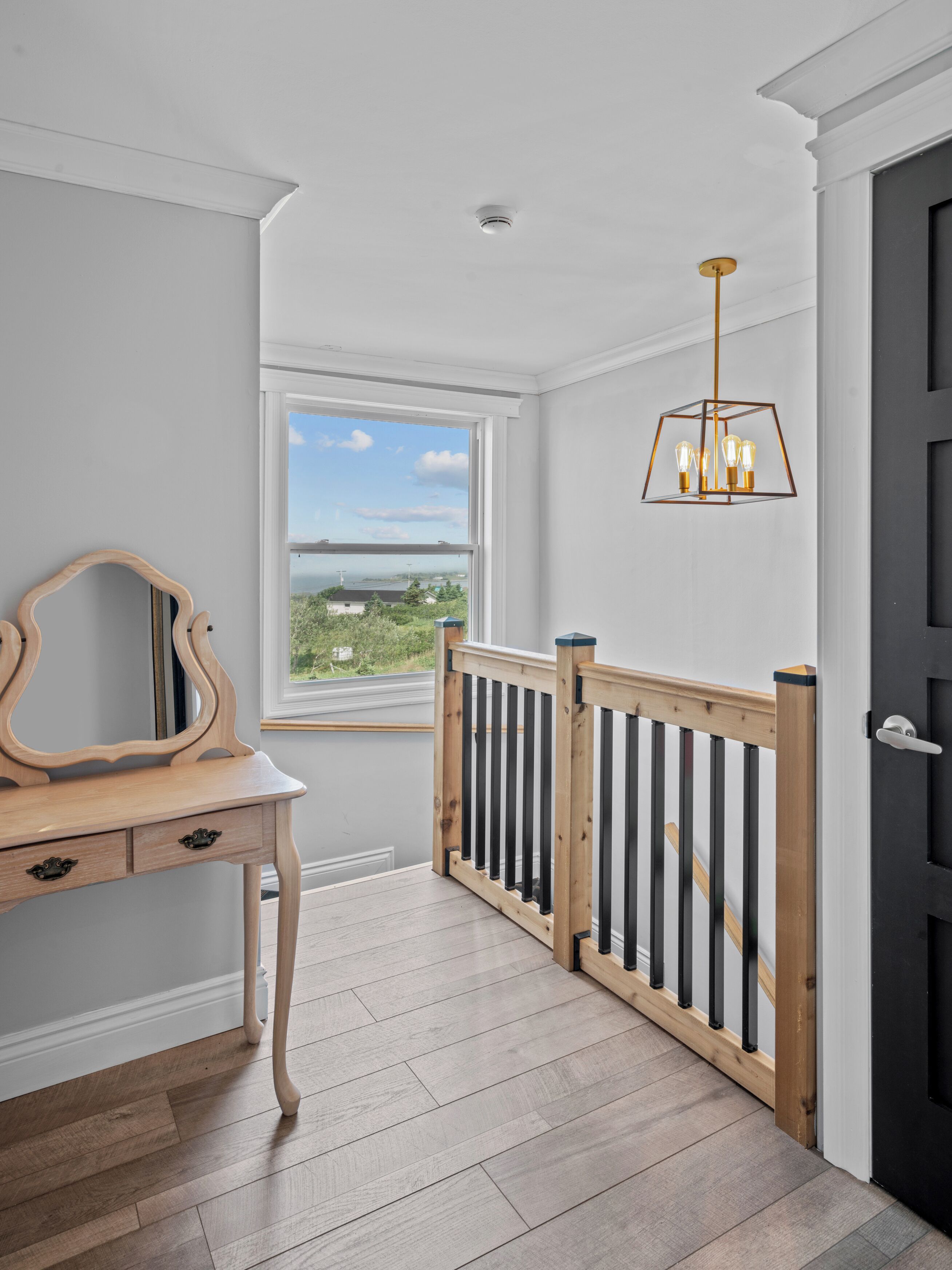 A room with a wooden desk, a window with a view, a black door, and a hanging light fixture.