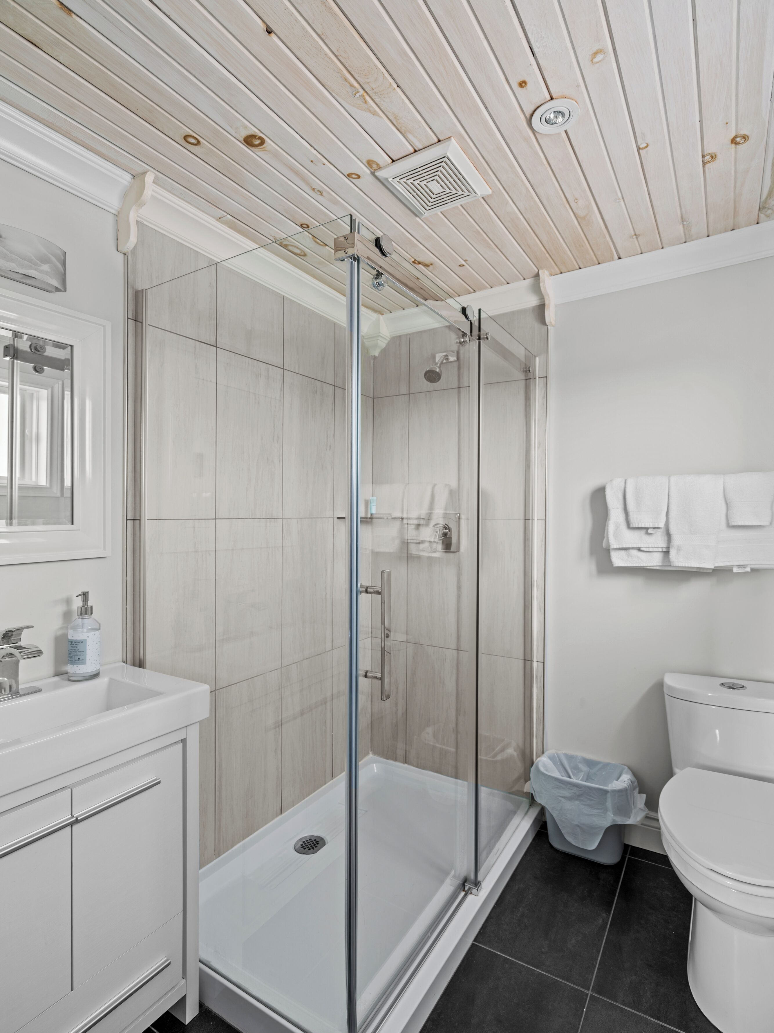Een moderne badkamer met een douche in een glazen cabine, witte kastjes en een toilet.