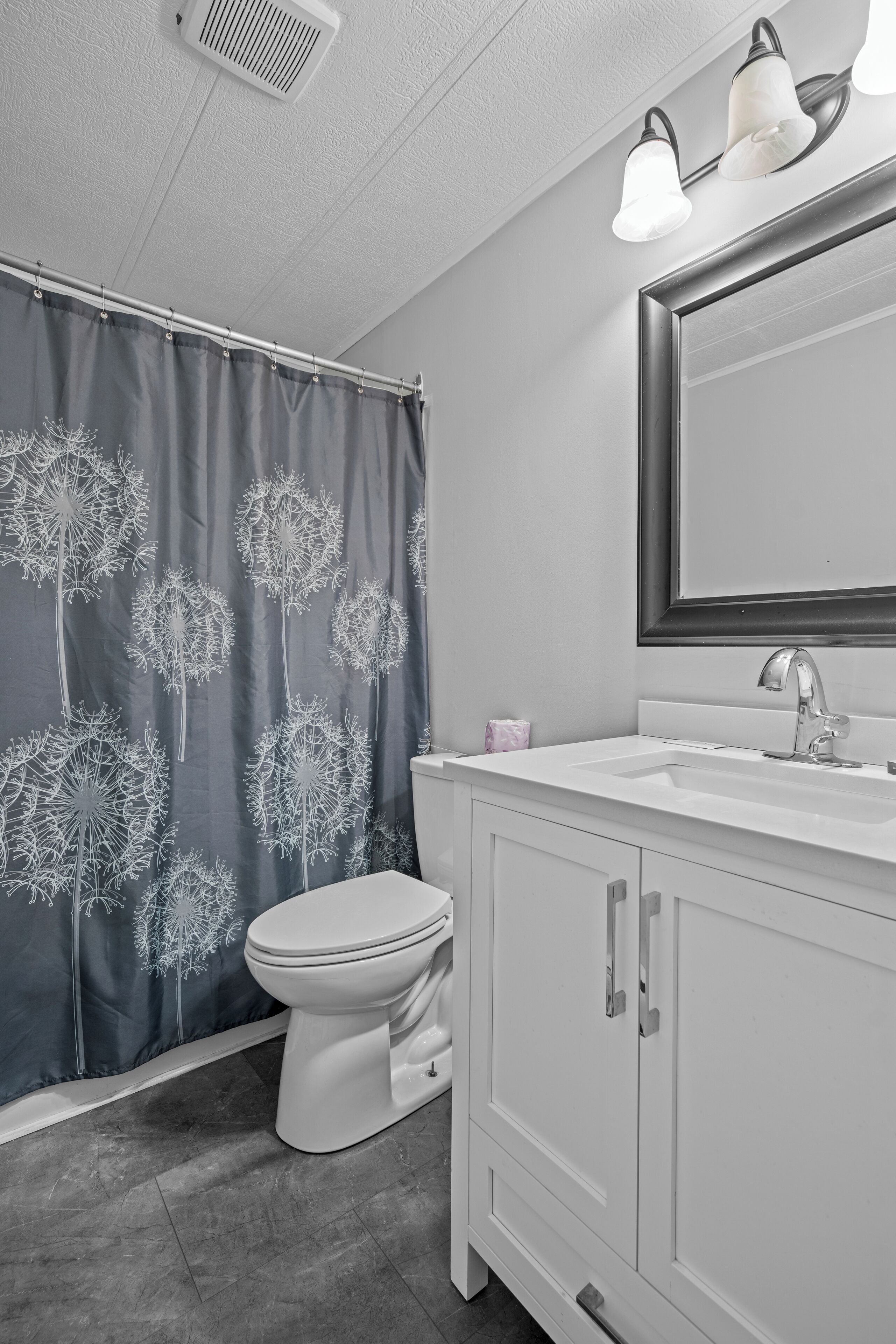 A bathroom with a white sink, a mirror, and a shower curtain with a dandelion pattern.