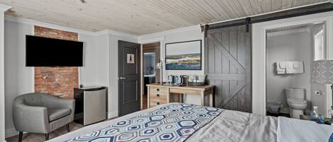 A modern bedroom with a bed, a desk, a chair, a TV, and a bathroom.