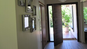 A hallway with multiple ornate mirrors on the wall, a wooden door, and a view of a garden through an open door. - The Pecan Tree (Sandton)