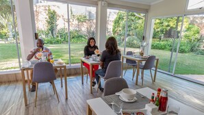 A dining area with large windows, wooden flooring, and a view of a garden. - The Pecan Tree (Sandton)