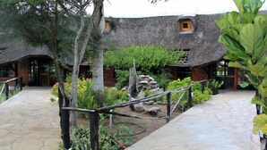 Un patio con un edificio de techo de paja, senderos de piedra y abundante vegetación.