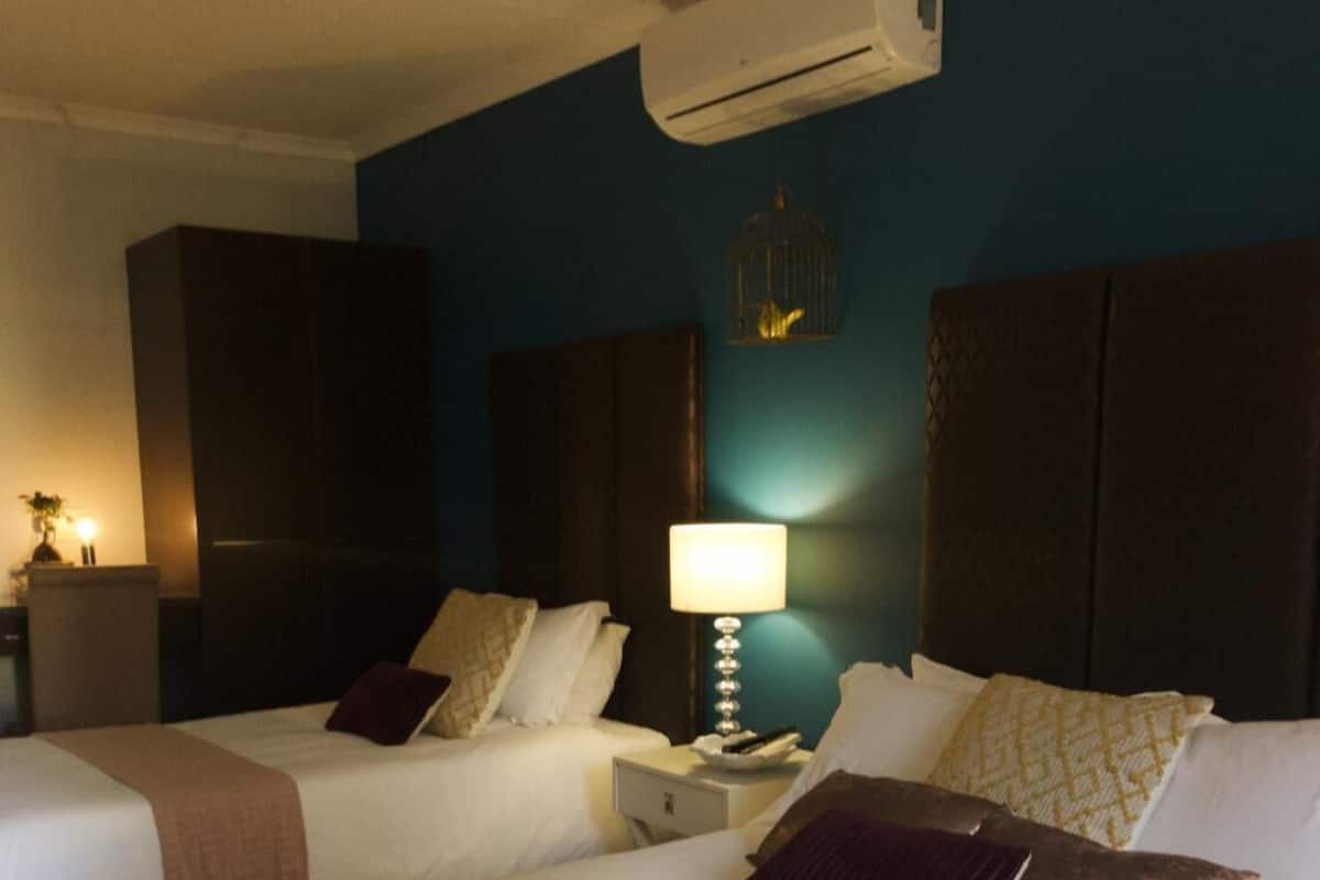 Habitación de hotel con dos camas, una mesita de noche, una lámpara y un equipo de aire acondicionado en la pared.