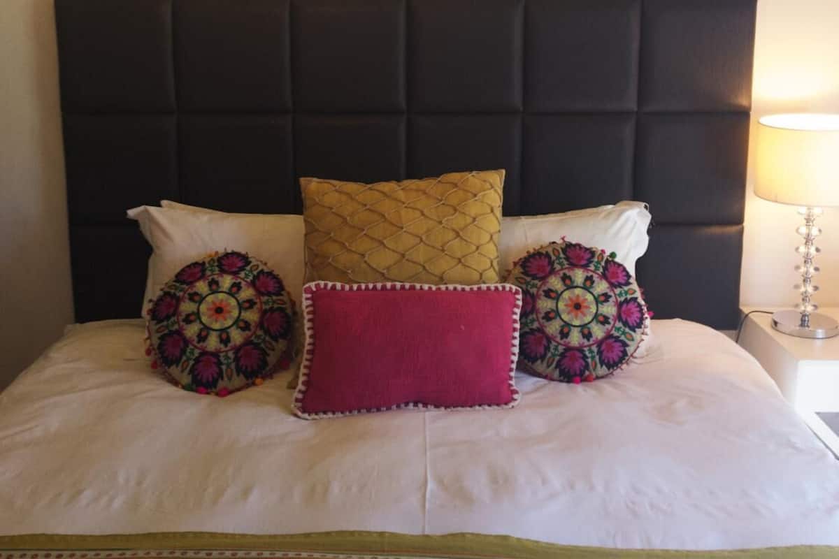 Una cama con cabecera negra, varios almohadones decorativos y una colcha estampada.