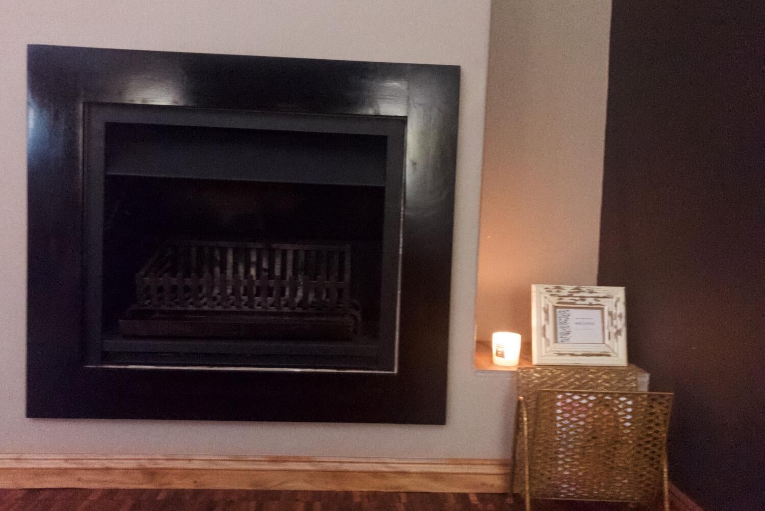 A fireplace with a dark frame, a lit candle, and a decorative box on a wooden floor.