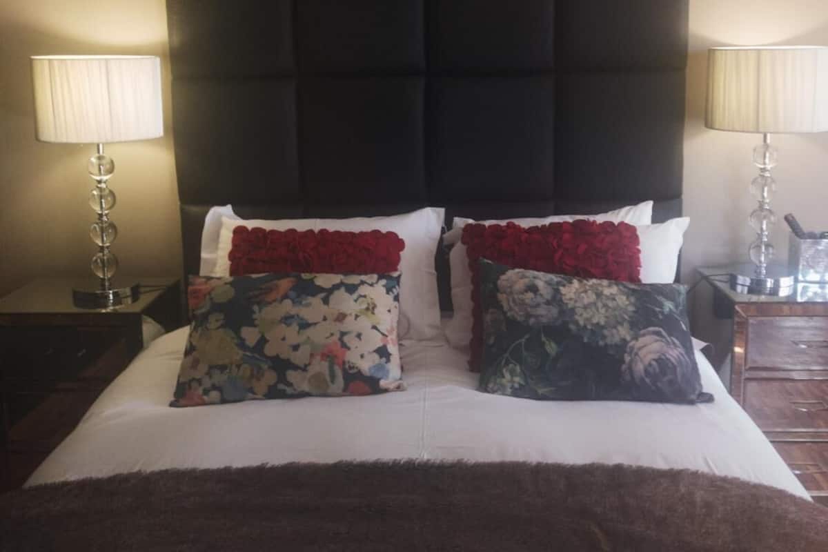 Una cama con cabecera oscura, dos mesitas de noche con lámparas y almohadas estampadas.