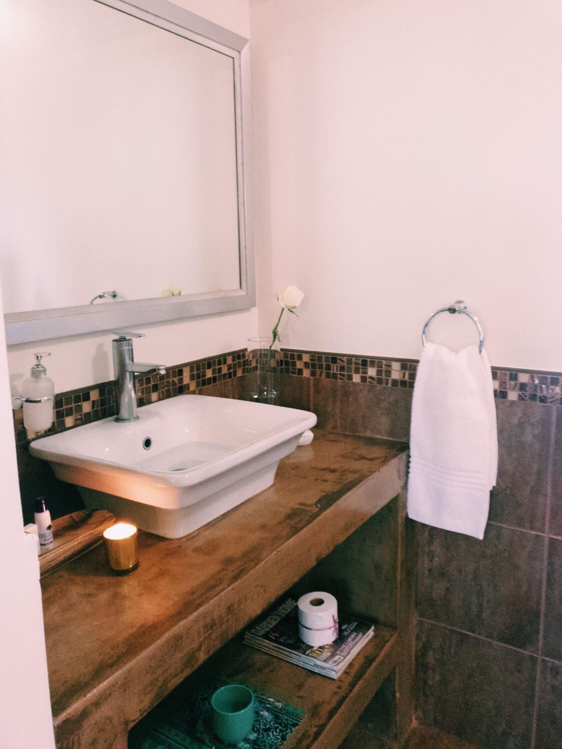 Un baño con un lavamanos grande, un espejo, un perchero para toallas y una vela pequeña.