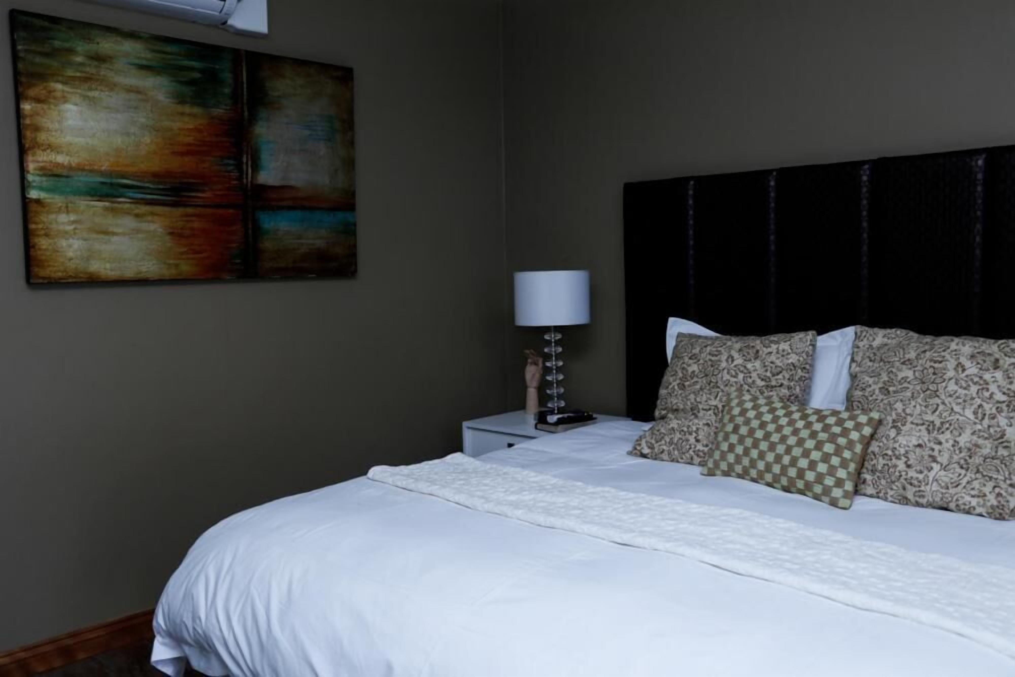 A neatly made bed with white linens, a dark headboard, and patterned pillows.