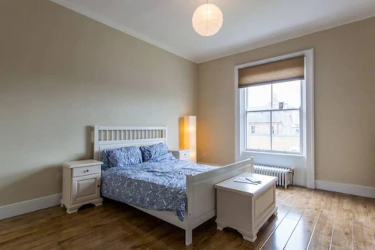 Un dormitorio con cama, mesitas de noche, un radiador y una ventana con vistas.