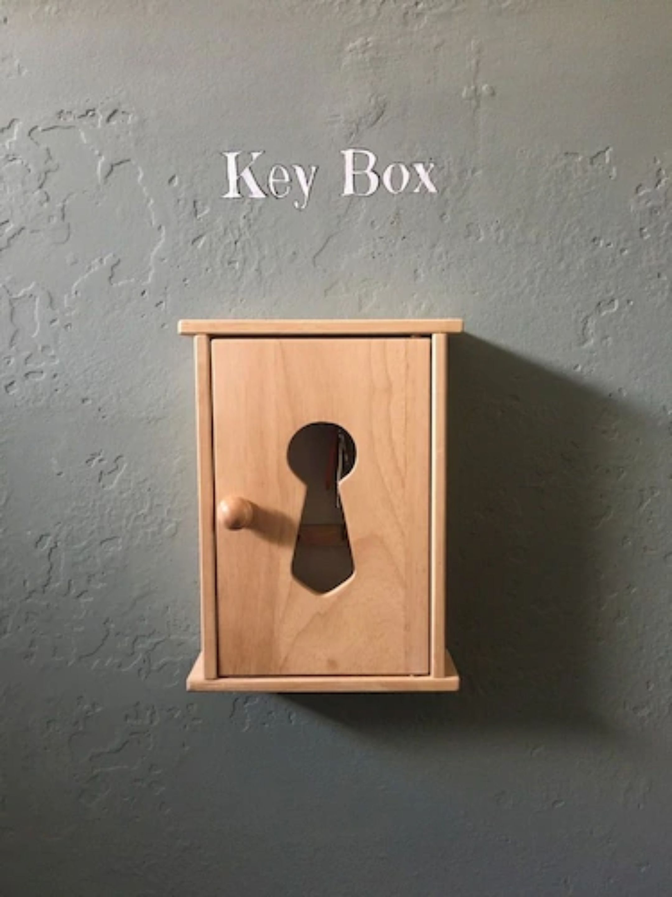 A wooden key box with a keyhole, mounted on a textured wall.