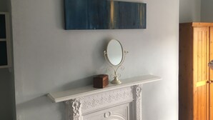 A room with a white fireplace, a decorative mirror, and a blue abstract painting on the wall. - Belvedere BnB (Dublin)