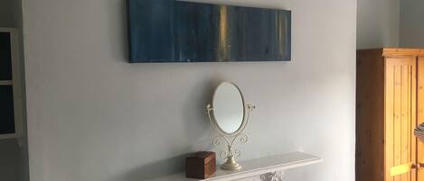 Um quarto com lareira branca, um espelho decorativo e uma pintura abstrata azul na parede.
