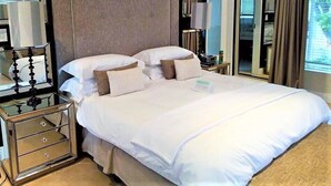A hotel room with a large bed, a nightstand with a mirror, and a bedside table with a lamp. - Q on First (Johannesburg)