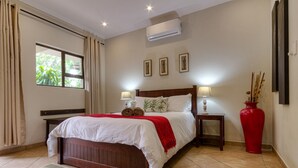 A neatly arranged bedroom with a wooden bed, two bedside tables with lamps, a red vase, and framed pictures on the wall. - Forest Villas (St. Lucia)