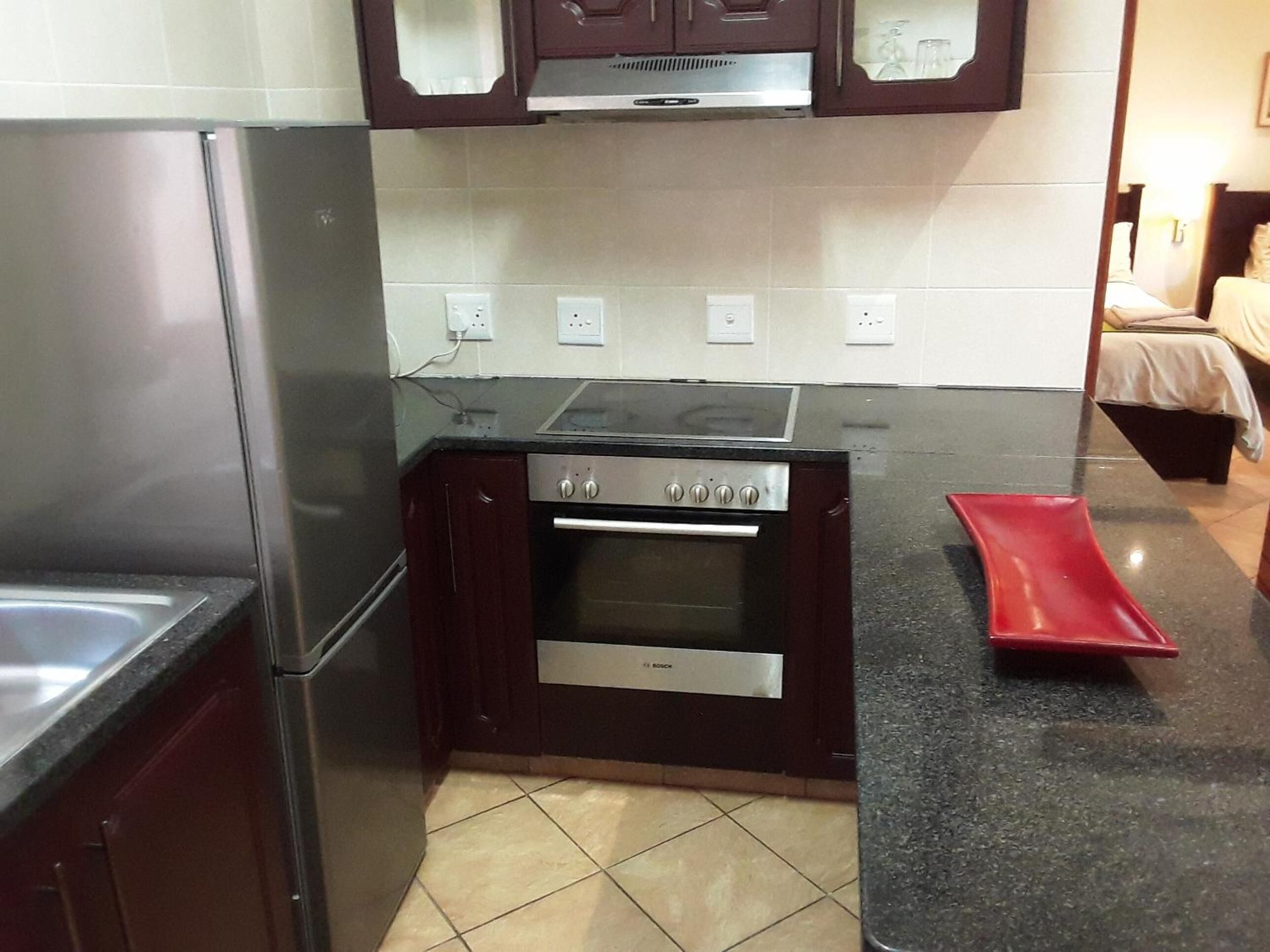 Una cocina compacta con horno Bosch, refrigerador de acero inoxidable y gabinetes de madera oscura.